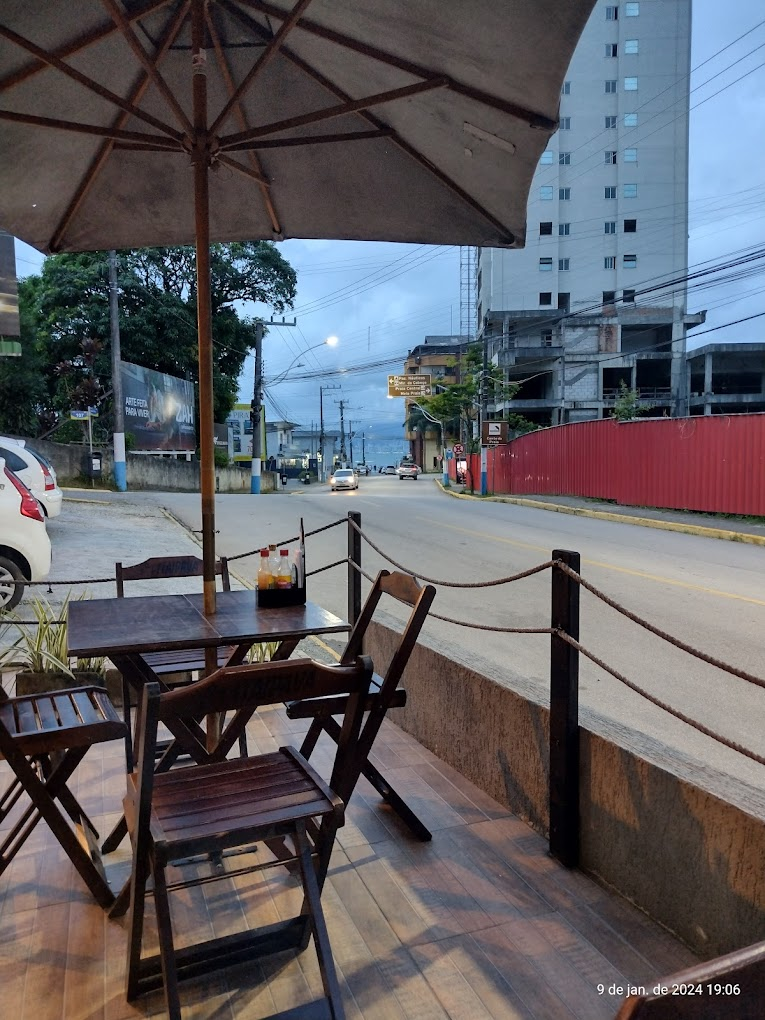 Espaço coberto do Vizinhos Espetinhos com lâmpadas pendentes, samambaias e mesas industriais